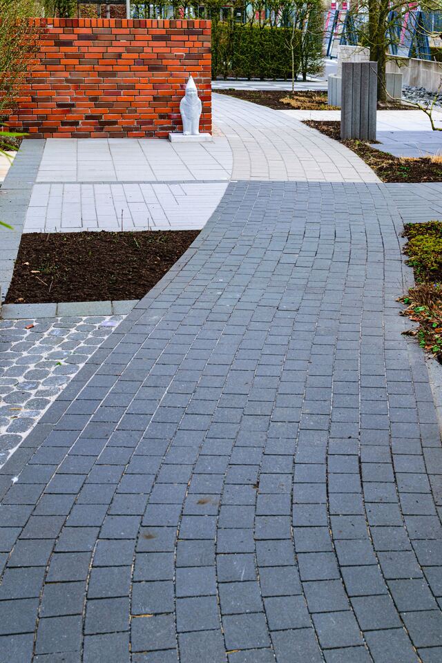 Een gebogen pad in grijze klinkers tussen borders en een gemetste tuinmuur